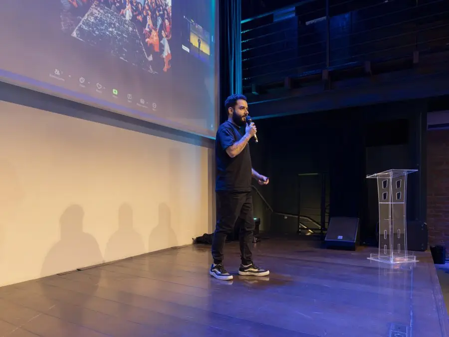 Palestrante no palco de um evento corporativo com telão ao fundo